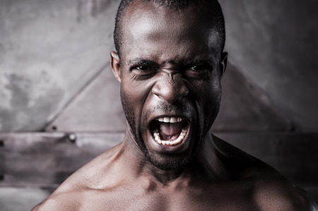 Furious and aggressive. Portrait of furious young shirtless African man shouting and looking at cameraの写真素材