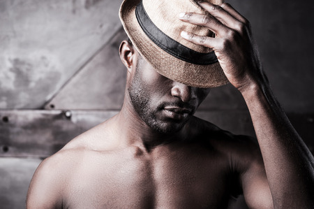 Wearing his favorite hat. Portrait of young shirtless African man adjusting his hat while standing against metal backgroundの写真素材