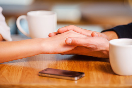 Enjoying their closeness. Close-up of couple holding hands while enjoying fresh coffee in cafe togetherの写真素材