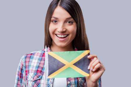 The are no boundaries for friendship. Happy young women flag of Jamaica while standing against grey backgroundの写真素材