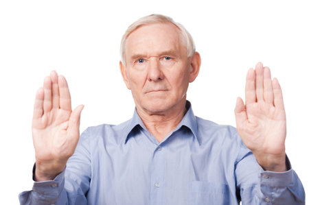 Stop it! Serious senior man in shirt showing his palms and looking at camera while standing against white backgroundの写真素材