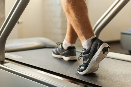 Exercising on treadmill. Close-up of man walking by treadmill in sports clubの写真素材