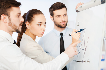 Discussing progress graph. Three confident business people discussing graph on the whiteboard while standing close to each otherの写真素材