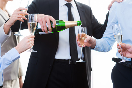 Celebrating success together. Close-up of business people holding flutes while man pouring champagneの写真素材