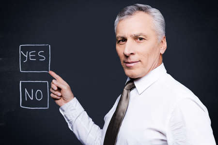Confident senior man in formalwear looking at camera and pointing chalk drawing on blackboardの写真素材
