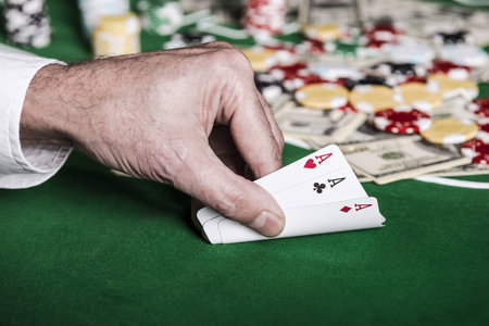 Nice combination. Close-up of male hand showing his cards on the poker table with chips and money...