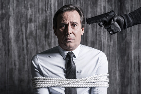 Please no! Tied up businessman caught by a criminal aiming his head with gunの写真素材
