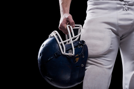 Cropped image of American football player holding football helmet while standing against black backgroundの写真素材