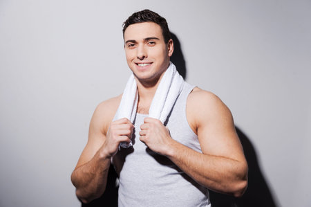 Handsome young man with towel on shoulders looking at camera and smiling while standing against grey backgroundの写真素材