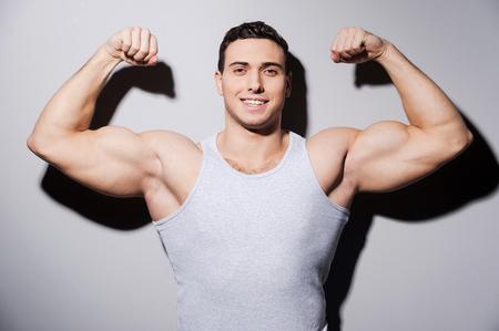  Young muscular man showing his biceps and smiling while standing against grey backgroundの写真素材