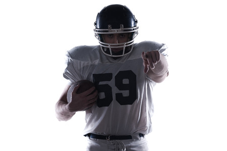 American football player holding ball and pointing at camera while standing against white backgroundの写真素材