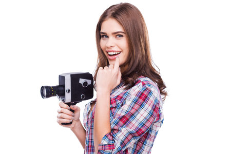 Beauty with movie camera. Cheerful young woman holding movie camera and smiling while standing...