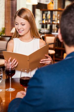Woman examining menu. Beautiful young loving couple sitting at the restaurant together while woman examining menu and smilingの写真素材