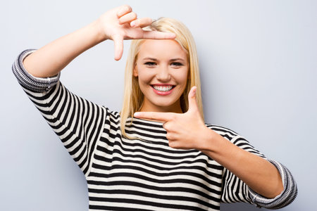 Gesturing finger frame. Beautiful young blond hair woman looking at camera and gesturing finger...