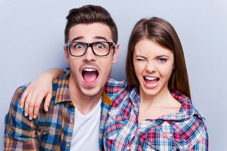 Playful couple. Beautiful young loving couple making faces at camera while standing against grey background Playful couple. Beautiful young loving couple making faces at camera while standing against grey background