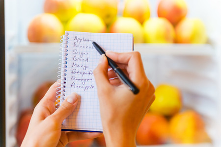 Checking shopping list. Close-up of woman checking shopping list with apples in the backgroundの写真素材
