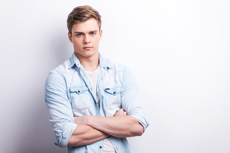Young and confident. Handsome young man keeping arms crossed while standing against grey background.の写真素材