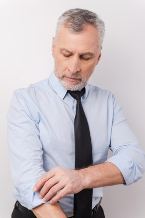 Ready to work. Confident grey hair senior man in formalwear adjusting his sleeve while standing against white backgroundの写真素材