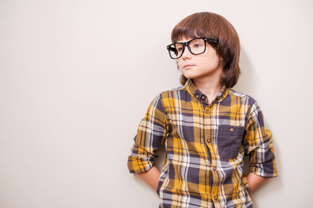 Full of inspiration. Little boy in eyewear leaning the wall and looking away while standing against...