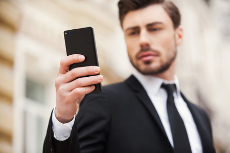 Always connected. Confident young man in formalwear holding mobile phone while standing outdoorsの写真素材
