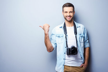 Photographers choosing it. Handsome young man with digital camera pointing away and smiling while...