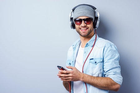 Listening to his favorite song. Handsome young stylish man in headphones holding MP3 Player and...