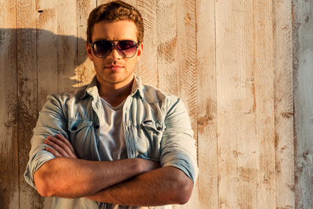 Fashionable and handsome. Handsome young man in sunglasses leaning at the wall and keeping arms crossedの写真素材
