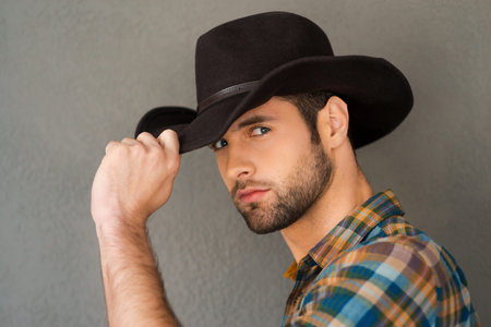 Wild West is his heart. Handsome young man adjusting his cowboy hat and looking at camera while...