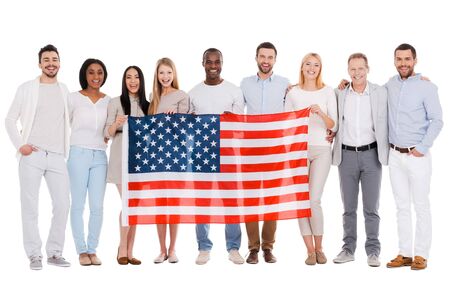 Team of America. Full length of happy diverse group of people bonding to each other and holding flag of America while standing against white background togetherの写真素材
