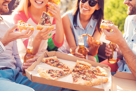 Pizza time! Close-up of four young cheerful people eating pizza and drinking beer outdoors Pizza time! Close-up of four young cheerful people eating pizza and drinking beer outdoors