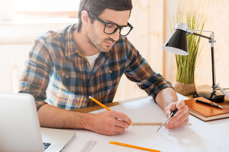 Bringing his ideas to life. Concentrated young man drawing while sitting at his working place