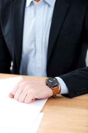 Time for business. Close-up of businessman wearing watch on his hand while sitting at his working placeの写真素材