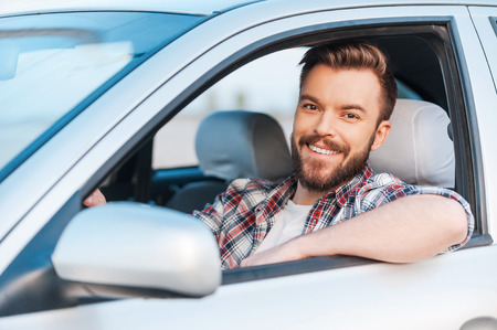 I love my car! Handsome young man driving his car and smiling at cameraの写真素材