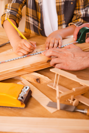 Skilled little carpenter.Seriousboy making measurements on the wooden plank while his father helping himの写真素材