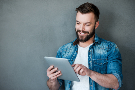 Technology takes you to the top. Happy young man holding digital tablet and smiling while standing against grey backgroundの写真素材