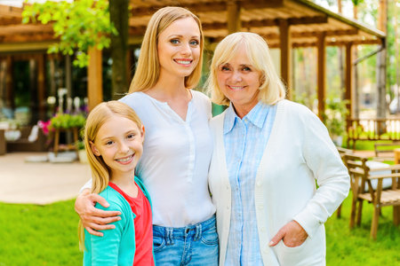 Three generations of family women bonding to each other and smiling while standing in front of their...