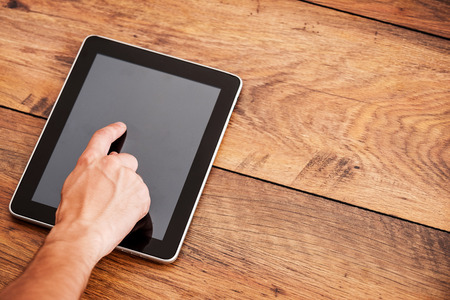 Close-up of man touching digital tablet laying on wooden deskの写真素材