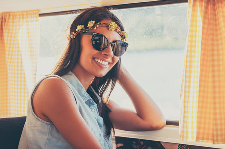 Flower child in the sun. Happy young woman smiling at camera while sitting inside of the retro vanの写真素材
