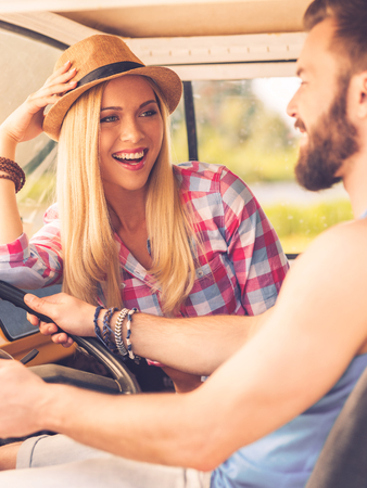 Enjoying simple pleasures. Happy young couple looking at each other with smiles while sitting inside of their minivanの写真素材