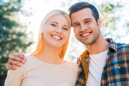 Beautiful and happy couple. Low angle view of beautiful young couple bonding to each other and smiling while standing outdoorsの写真素材