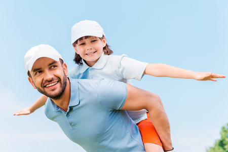 Having fun together. Cheerful young man carrying his son on shoulders while standing outdoorsの写真素材