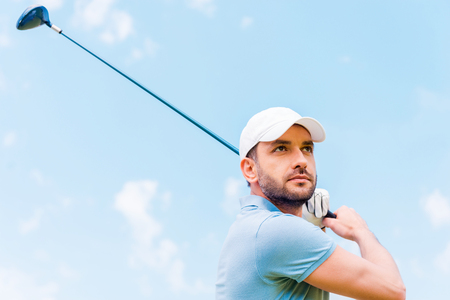 Confident golfer. Low angle view of serious young man playing golf while standing outdoorsの写真素材