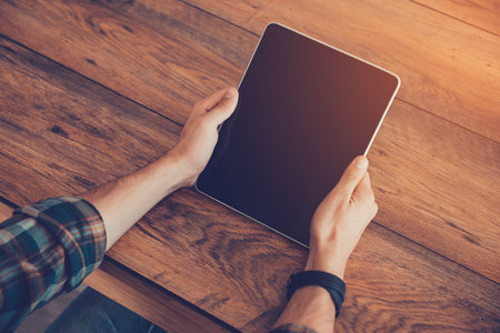 Device for easyier life. Top view of man holding digital tablet while sitting at the wooden desk