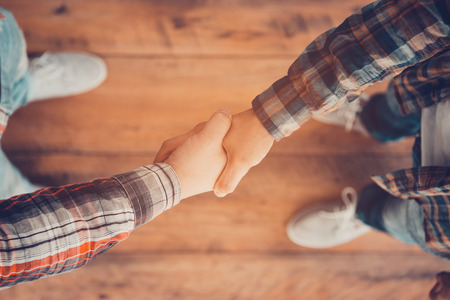 Men shaking hands. Top view of two men shaking hands while standing on the wooden floorの写真素材