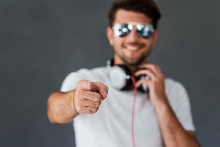 Do you like my style? Happy young man in headphones pointing you and smiling while standing against grey backgroundの写真素材