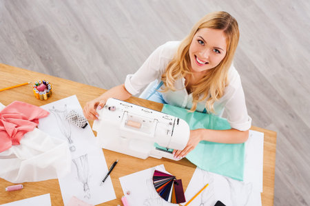 Fashion designer at work. Top view of cheerful young woman sewing while sitting at her working place...