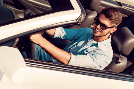Perfect day for driving. Top view of happy young man looking forward and smiling while driving his...