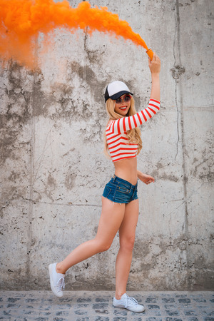 Lighting up this day. Happy young women holding smoke bomb and smiling while posing against the concrete wallの写真素材