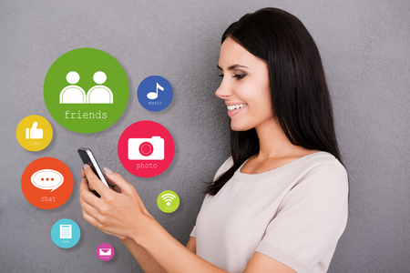 Cheerful young woman holding smart phone with colorful icons around itの写真素材