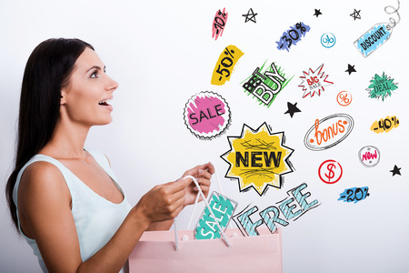 Side view of surprised young woman in dress carrying shopping bag and looking at the colorful sketchesの写真素材